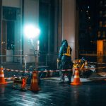 Trabalhadores da construção caminham à noite em uma área urbana iluminada.