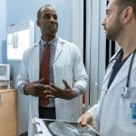 Dois médicos de jaleco analisam uma radiografia em um ambiente clínico.