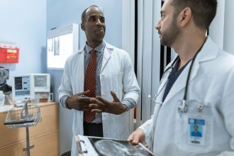 Dois médicos de jaleco analisam uma radiografia em um ambiente clínico.