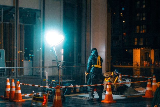 Trabalhadores da construção caminham à noite em uma área urbana iluminada.