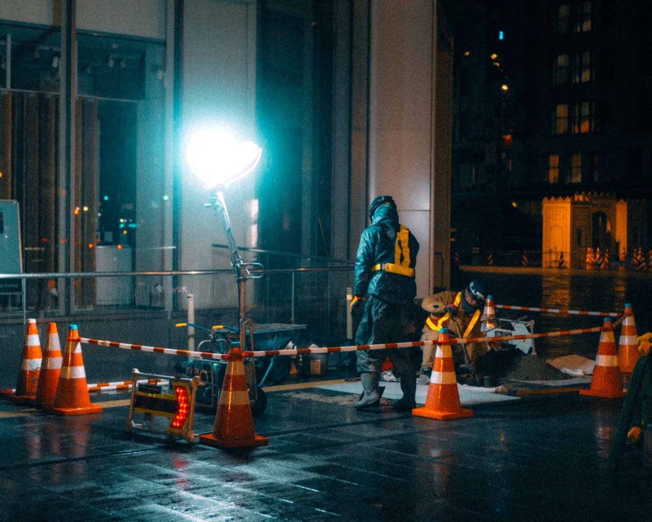 Trabalhadores da construção caminham à noite em uma área urbana iluminada.