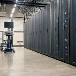 Armários metálicos com servidores, equipamentos de rede e cabos em um datacenter moderno.
