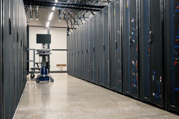Armários metálicos com servidores, equipamentos de rede e cabos em um datacenter moderno.
